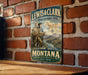 A vintage metal sign for the Lewis & Clark National Historic Trail in Montana, featuring two men on a mountain trail with a scenic landscape in the background.