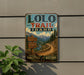 A vintage-style metal sign for the Lolo Trail in Idaho, featuring a scenic mountain landscape with a winding trail and a sign indicating the trail's name.