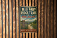 A vintage metal sign for the "MILITARY RIDGE TRAIL" in Wisconsin, featuring a scenic landscape with a winding path and a signpost.