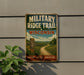 A vintage metal sign for the "MILITARY RIDGE TRAIL" in Wisconsin, featuring a scenic landscape with a dirt path and a signpost.