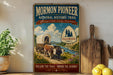 A vintage-style sign for the Mormon Pioneer National Historic Trail, featuring an illustration of a wagon train traveling through a scenic landscape with a river and mountains in the background.