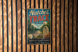A vintage metal sign for Natchez Trace, a scenic journey in Alabama, is displayed on a wooden wall.