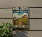 a vintage-style sign for the North Country National Scenic Trail in North Dakota, with a mountain landscape and trail marker in the background.