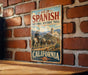 A vintage metal sign for the Old Spanish National Historic Trail in California, featuring an illustration of a cowboy on a horse and a desert landscape.