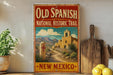a vintage-style sign for the Old Spanish National Historic Trail in New Mexico, with a desert landscape and a church in the background.
