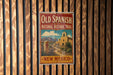A vintage-style sign for the "Old Spanish National Historic Trail" in New Mexico, featuring a desert landscape with a church and mountains in the background.