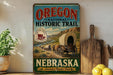 a vintage-style sign for Oregon National Historic Trail, with a wagon train depicted on the sign. The sign is displayed on a shelf next to a wooden cutting board and a potted plant.