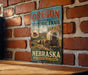 A vintage-style metal sign for the Oregon National Historic Trail in Nebraska, featuring an illustration of a wagon train traveling through the state.