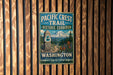 A vintage-style metal sign for the Pacific Crest Trail Historic Corridor in Washington, featuring a mountain landscape and a trail marker.