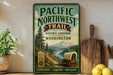 a vintage-style metal sign for the Pacific Northwest Trail, with a scenic illustration of a trail surrounded by mountains, pine trees, and a wagon. The sign is displayed on a shelf next to a wooden cutting board and a potted plant.