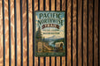 A vintage-style metal sign for the Pacific Northwest Trail Historic Corridor Washington, featuring a wagon train and a mountain landscape.