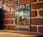 A vintage-style metal sign for the Santa Fe National Historic Trail in Colorado, featuring a wagon train and mountains in the background.