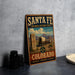 A vintage-style metal sign for the Santa Fe National Historic Trail in Colorado, featuring an illustration of a wagon train on a trail surrounded by mountains.