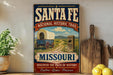 A vintage-style sign for the National Historic Trail in Missouri, featuring an illustration of a wagon on a dirt road and a monument.