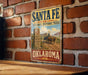 A vintage-style metal sign for the Santa Fe National Historic Trail in Oklahoma, featuring an illustration of a wagon train on a dirt road.