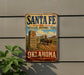 A vintage-style metal sign for the Santa Fe National Historic Trail in Oklahoma, featuring a wagon and a desert landscape.