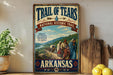 A vintage-style poster for the Trail of Tears, a historic event in Arkansas, featuring a group of people in traditional clothing walking along a path through a scenic landscape.