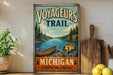 A vintage-style metal sign advertising the Michigan Voyageurs Trail, featuring a scenic illustration of a canoe on a lake surrounded by pine trees.