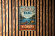 A vintage-style metal sign with the text "VOYAGEURS TRAIL" and "MICHIGAN Explore the Legacy" is displayed on a wooden wall.