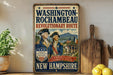 A vintage-style metal sign with the text "WASHINGTON-ROCCHAMBEAU REVOLUTIONARY ROUTE" and an illustration of two men in military uniforms, along with the text "LIBERTY REVOLUTIONARY VICTORY" and "A PATH OF ALLIANCE A LEGACY OF FREEDOM" in the foreground. The sign is displayed on a shelf next to a wooden cutting board and a potted plant.