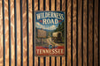 A vintage-style metal sign that reads "Wilderness Road" and "The Historic Trail That Opened the West" is displayed on a wooden wall.