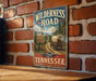 A vintage-style metal sign for the Wilderness Road in Tennessee, featuring a wagon train and a sign that says "The Historic Trail That Opened the Way to the West".
