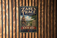 A vintage-style metal sign with the text "Zane's Trace" and "OHIO" is displayed on a wooden wall.