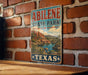 A vintage-style sign for Abilene State Park in Texas, featuring a scenic landscape with mountains, water, and desert vegetation.
