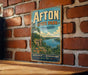 A vintage-style metal sign for Afton State Park in Minnesota, featuring a scenic landscape with a lake, mountains, and a sailboat.