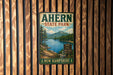 A vintage metal sign for Ahern State Park in New Hampshire, featuring a scenic landscape with a lake, mountains, and pine trees.