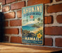 A vintage-style metal sign with the text "AHUKINI RECREATION AREA STATE PARK HAWAII E REMO MA!" displayed on a brick wall.