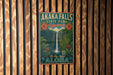 A vintage-style metal sign for Akaka Falls State Park in Hawaii, featuring a waterfall and tropical foliage, is displayed on a wooden wall.