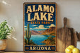 A vintage-style sign for Alamo Lake State Park in Arizona, featuring a desert landscape with a cactus and a lake.