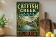 A vintage-style metal sign for Catfish Creek Preserve in Florida, featuring a large blue heron in the foreground and a serene landscape of a river and trees in the background.