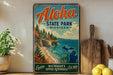 A vintage-style metal sign for Aloha State Park in Michigan, featuring a scenic coastal landscape with cliffs, pine trees, and a lake.