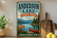 A vintage-style sign for Anderson Lake State Park in Washington, featuring a scenic image of a lake, mountains, and a canoe.