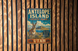 A vintage metal sign for Antelope Island State Park in Utah, featuring an illustration of a mountain and a gazelle.