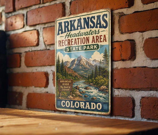 A vintage metal sign for Arkansas Headwaters Recreation Area in Colorado, featuring a scenic mountain landscape with a river and pine trees.