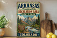 A vintage-style sign for Arkansas Headwaters Recreation Area in Colorado, featuring a scenic mountain landscape with a river flowing through it.