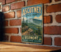 A vintage metal sign for Ascutney State Park in Vermont, featuring a scenic mountain landscape and the words "Explore, Relax, Discover" below.
