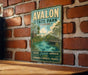 A vintage-style metal sign for "Avalon State Park, Florida" is displayed on a brick wall, featuring a scenic illustration of a river, palm trees, and a bridge.