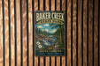 A vintage-style metal sign for Baker Creek State Park, featuring a scenic landscape with a waterfall and forest, mounted on a wooden wall.