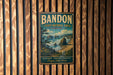 A vintage metal sign for Bandon State Natural Area in Oregon, featuring a scenic landscape with a beach, mountains, and a forest.