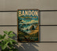 A vintage-style metal sign for Bandon State Natural Area in Oregon, featuring a scenic landscape with rocky cliffs, a beach, and a forest.