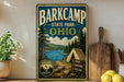 A vintage-style metal sign for Barkcamp State Park in Ohio, featuring a scenic landscape with pine trees, a lake, and a tent, along with the text "BARKCAMP STATE PARK OHIO" and "NATURE AWAITS".