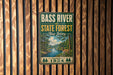A vintage metal sign for the Bass River State Forest in New Jersey, featuring a scenic illustration of a forest and a river.