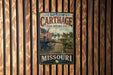 A vintage metal sign displaying the Battle of Cartage, a significant event in Missouri's state history, with an American flag in the background.