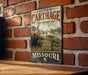 A vintage metal sign depicting a battle scene with soldiers and cannons, mounted on a brick wall.