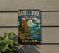A vintage metal sign for Battle Rock State Park in Oregon, featuring a scenic landscape with a mountain, river, and pine trees.