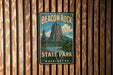 A vintage-style sign for Beacon Rock State Park in Washington, featuring a mountain landscape with a lake and pine trees.